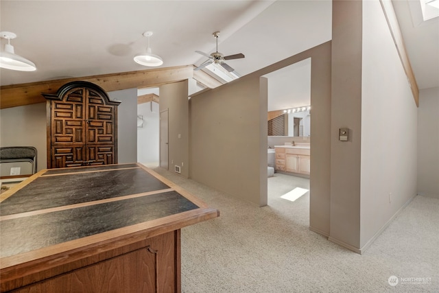 interior space featuring ceiling fan, sink, vaulted ceiling with skylight, and light colored carpet