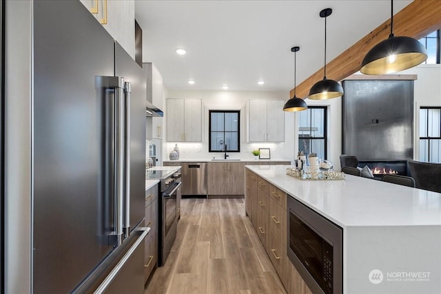 kitchen featuring pendant lighting, appliances with stainless steel finishes, a center island, sink, and light wood-type flooring