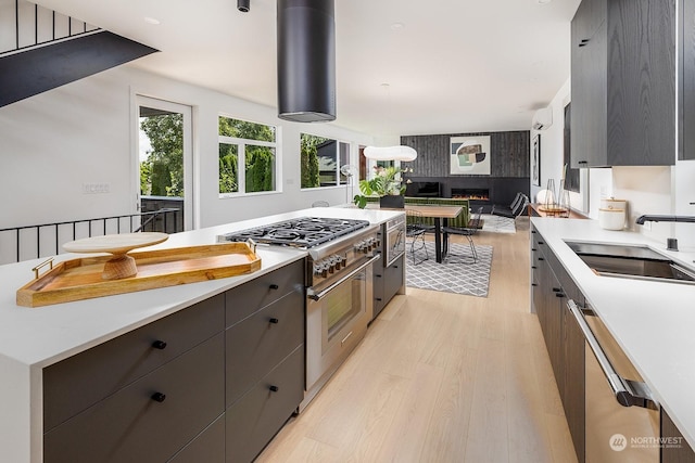 kitchen featuring sink, appliances with stainless steel finishes, a wall unit AC, light hardwood / wood-style floors, and a large fireplace