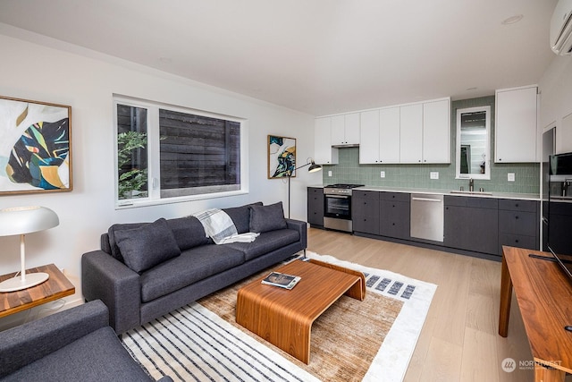 living room with an AC wall unit, plenty of natural light, sink, and light wood-type flooring