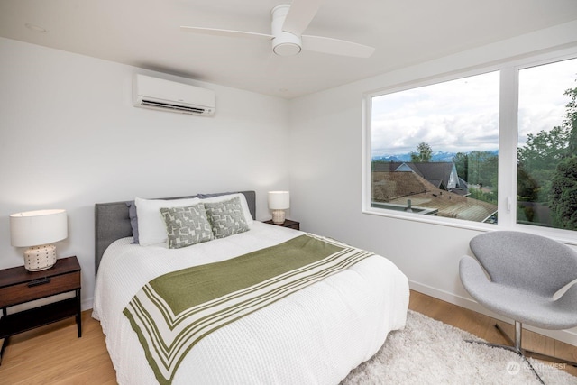 bedroom with ceiling fan, a wall unit AC, and light hardwood / wood-style flooring