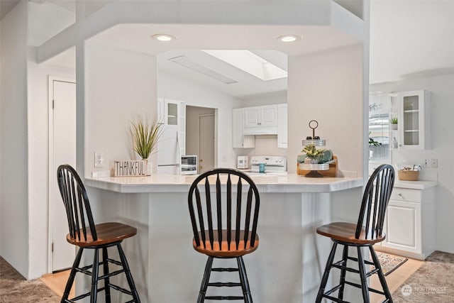 kitchen with glass insert cabinets, light countertops, white cabinetry, and a peninsula