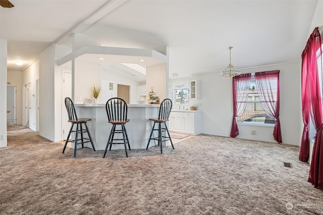 kitchen with lofted ceiling, light colored carpet, a peninsula, white cabinets, and a kitchen breakfast bar