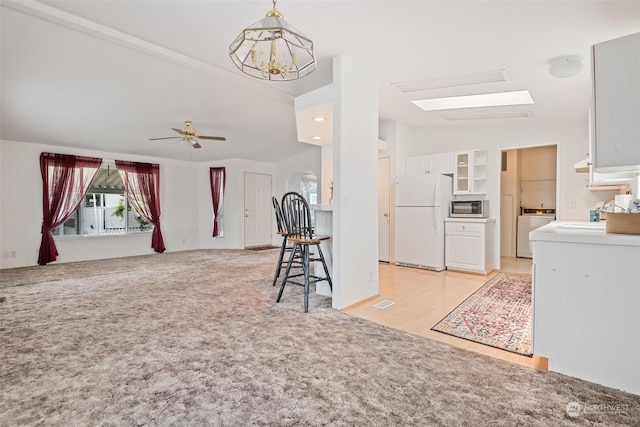 living room featuring lofted ceiling with skylight, washer / dryer, light colored carpet, and ceiling fan with notable chandelier