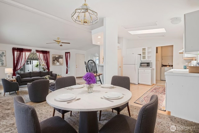 dining room with lofted ceiling with skylight, washer / clothes dryer, and ceiling fan with notable chandelier