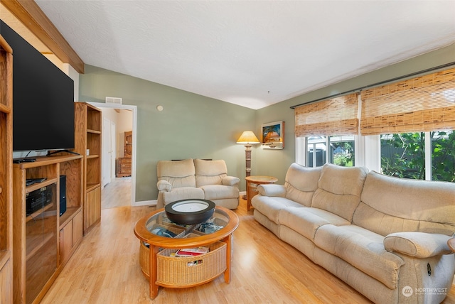 living area featuring visible vents, baseboards, lofted ceiling, light wood-style flooring, and a textured ceiling