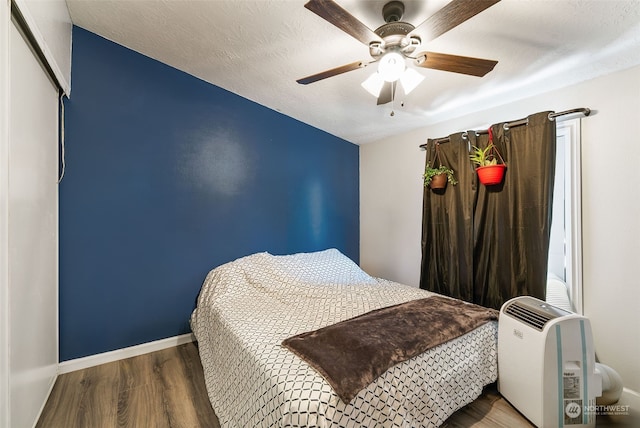 bedroom with a textured ceiling, wood finished floors, a ceiling fan, and baseboards