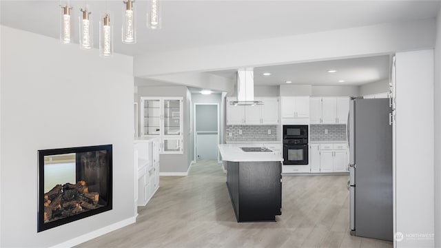 kitchen featuring black appliances, light hardwood / wood-style flooring, hanging light fixtures, and ventilation hood