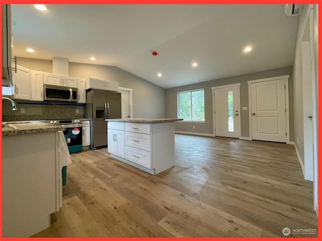 kitchen with appliances with stainless steel finishes, white cabinetry, light wood-type flooring, and lofted ceiling