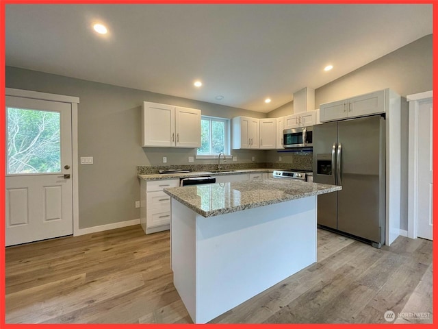 kitchen featuring appliances with stainless steel finishes, light wood-style floors, lofted ceiling, and a sink