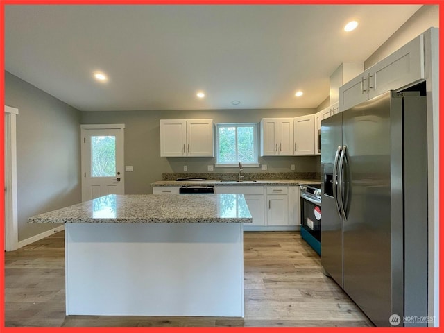 kitchen featuring a sink, a kitchen island, stainless steel appliances, white cabinets, and light wood finished floors