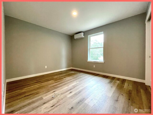 spare room with a wall mounted AC, baseboards, and wood finished floors