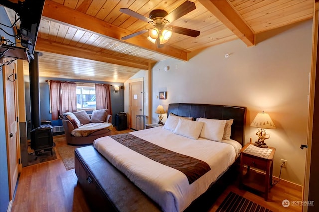 bedroom featuring hardwood / wood-style floors, wood ceiling, a wood stove, ceiling fan, and beam ceiling