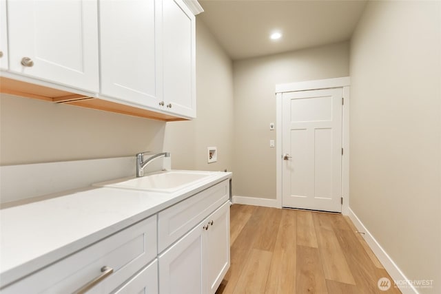 laundry room featuring hookup for a washing machine, cabinet space, a sink, light wood-type flooring, and baseboards