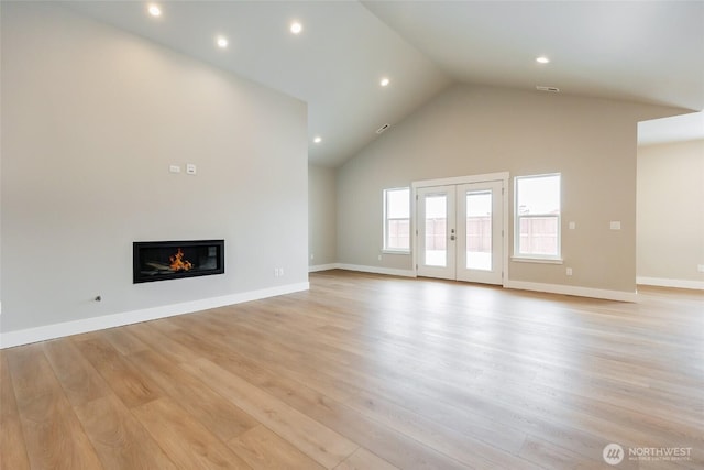 unfurnished living room featuring high vaulted ceiling, light wood-style flooring, baseboards, french doors, and a glass covered fireplace