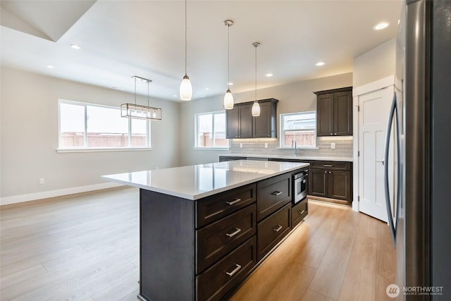 kitchen with a center island, light countertops, appliances with stainless steel finishes, decorative backsplash, and pendant lighting