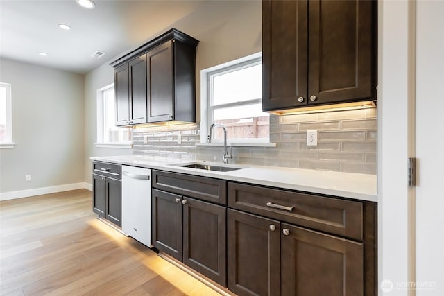 kitchen with light countertops, backsplash, dark brown cabinetry, white dishwasher, and a sink