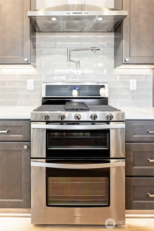 kitchen featuring range with two ovens, light countertops, wall chimney range hood, and tasteful backsplash