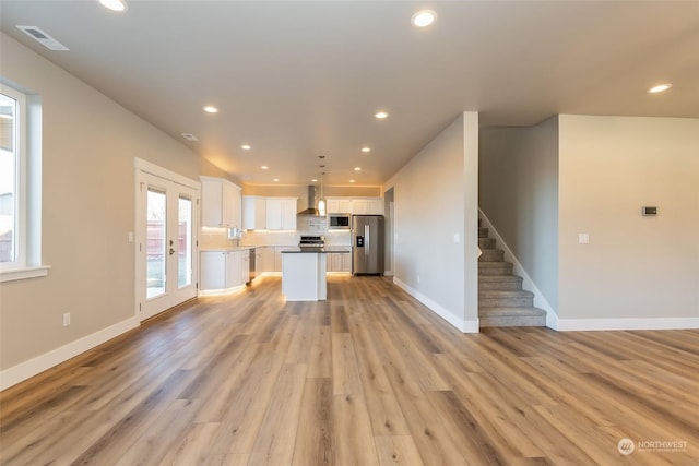 kitchen with a center island, white cabinets, wall chimney range hood, light hardwood / wood-style floors, and stainless steel appliances