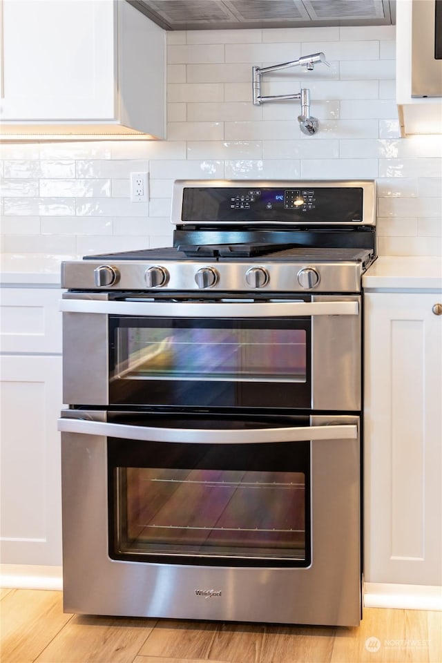 kitchen with decorative backsplash, white cabinets, light hardwood / wood-style floors, and stainless steel range oven