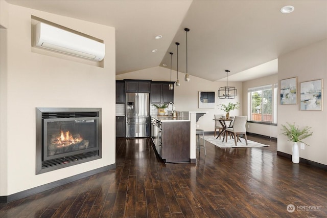 kitchen featuring pendant lighting, stainless steel refrigerator with ice dispenser, a wall mounted air conditioner, an island with sink, and dark hardwood / wood-style flooring