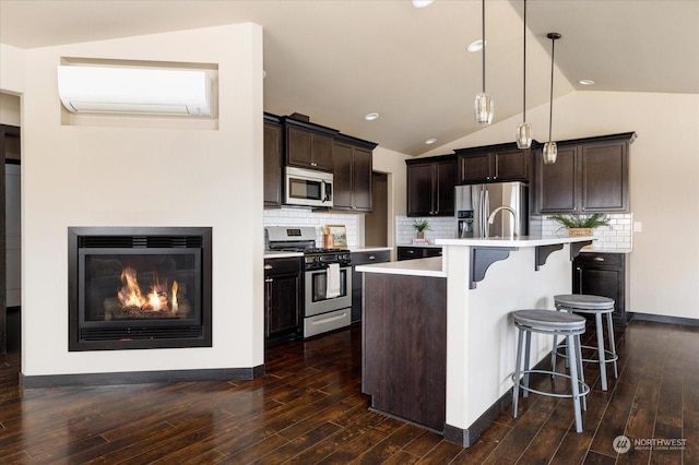 kitchen featuring appliances with stainless steel finishes, hanging light fixtures, a kitchen island with sink, light countertops, and a wall mounted AC