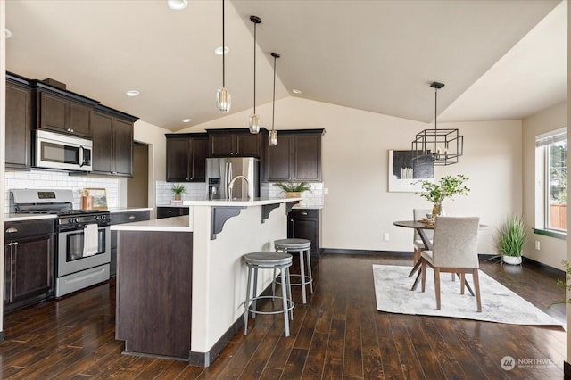 kitchen featuring stainless steel appliances, lofted ceiling, a kitchen island with sink, and decorative light fixtures