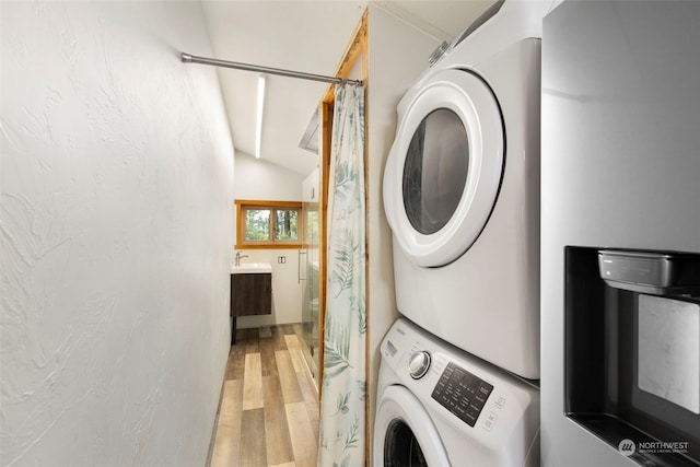 clothes washing area with stacked washer / drying machine, sink, and light hardwood / wood-style floors