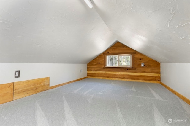 bonus room featuring lofted ceiling, carpet, and wood walls