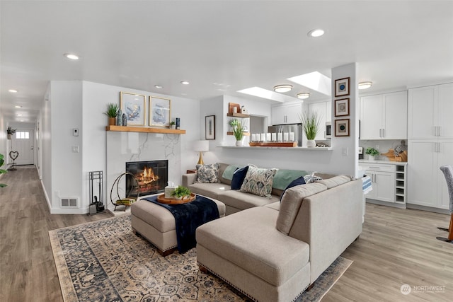 living room with a skylight, light hardwood / wood-style floors, and a premium fireplace