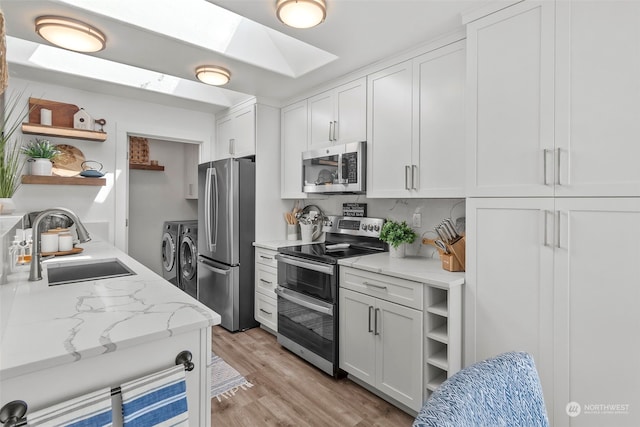 kitchen with sink, appliances with stainless steel finishes, white cabinetry, a skylight, and washer and dryer