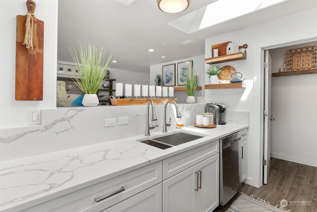 kitchen featuring a skylight, tasteful backsplash, sink, stainless steel dishwasher, and light stone countertops