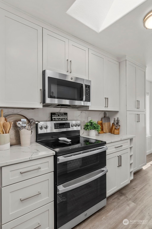 kitchen featuring white cabinetry, light stone counters, light hardwood / wood-style flooring, and stainless steel appliances