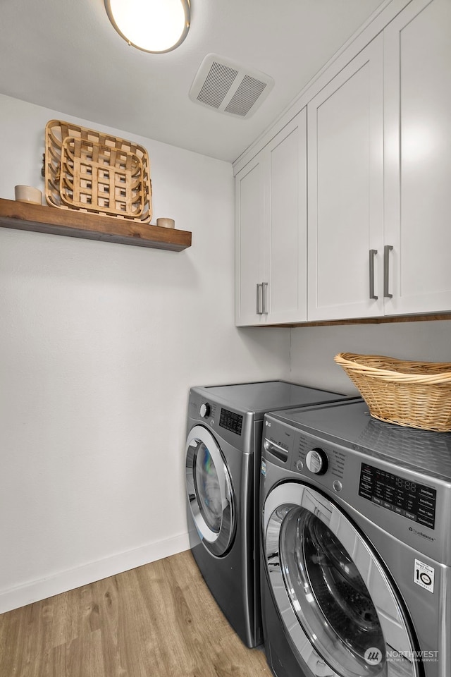 laundry area with cabinets, washing machine and dryer, and light wood-type flooring