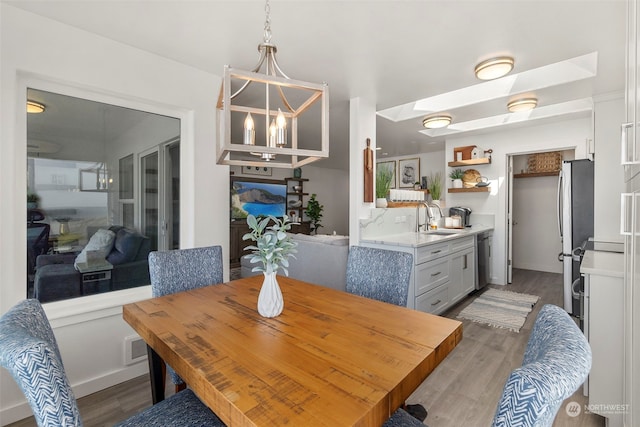 dining area with sink, hardwood / wood-style floors, an inviting chandelier, and a skylight