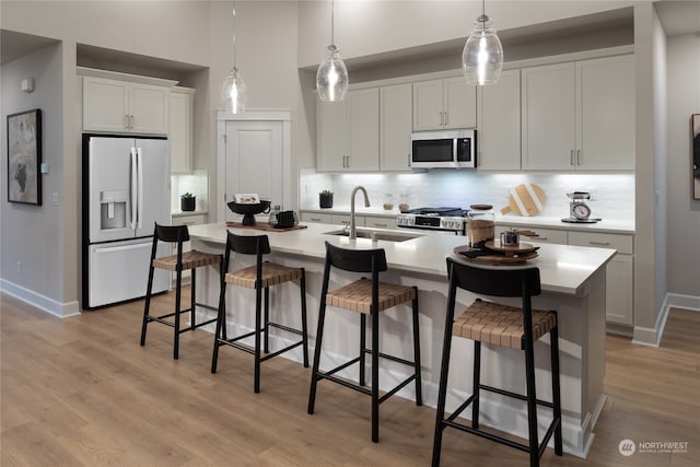 kitchen featuring stainless steel appliances, white cabinets, an island with sink, backsplash, and light hardwood / wood-style flooring