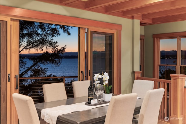 dining space with beam ceiling and a water view