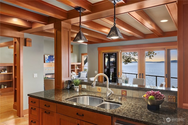 kitchen featuring sink, light wood-type flooring, hanging light fixtures, dark stone counters, and a water view