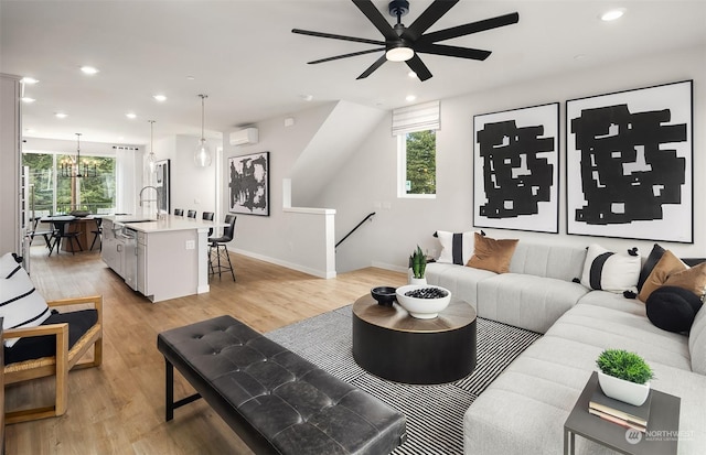 living room featuring light wood-type flooring, plenty of natural light, sink, and ceiling fan with notable chandelier