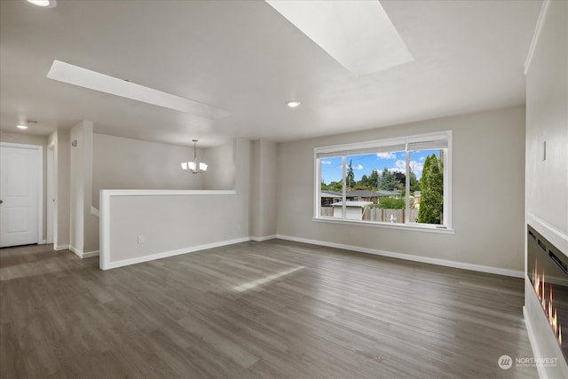 unfurnished living room featuring dark wood-type flooring, a skylight, and a notable chandelier