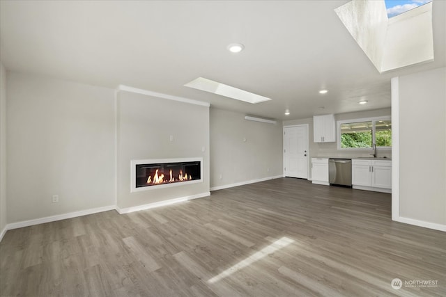 unfurnished living room with sink, hardwood / wood-style flooring, and a skylight