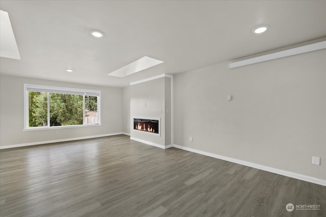 unfurnished living room featuring dark wood-type flooring and a skylight