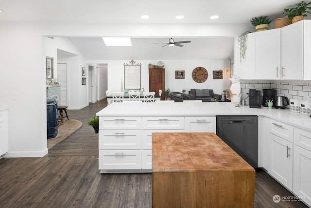 kitchen featuring kitchen peninsula, white cabinets, dishwasher, and a wood stove