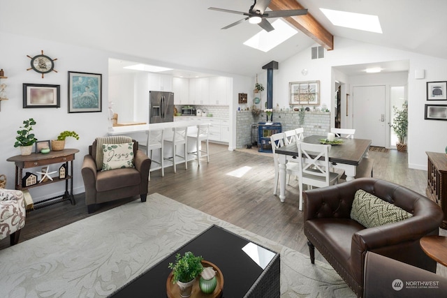 living room with ceiling fan, lofted ceiling with skylight, hardwood / wood-style floors, and a wood stove