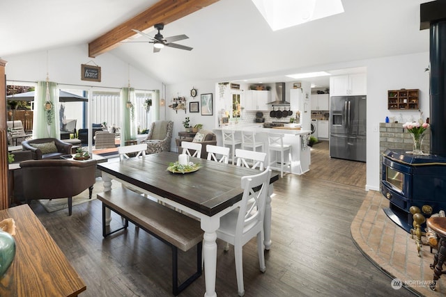 dining room featuring vaulted ceiling with skylight, ceiling fan, a wood stove, and dark hardwood / wood-style floors