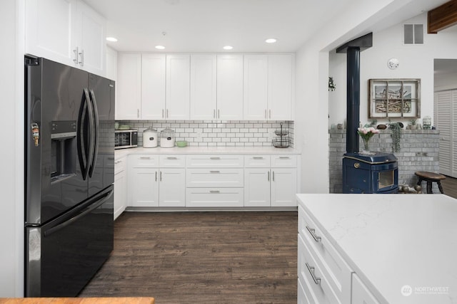 kitchen with dark wood-type flooring, a wood stove, white cabinets, black refrigerator with ice dispenser, and backsplash