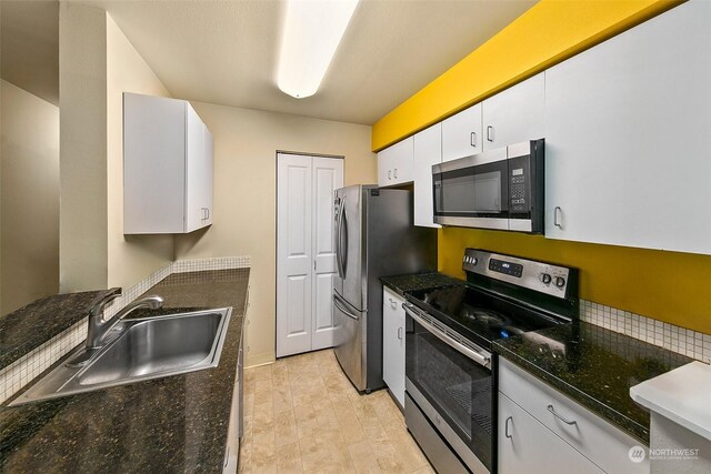 kitchen with dark stone counters, light tile patterned flooring, white cabinets, sink, and appliances with stainless steel finishes