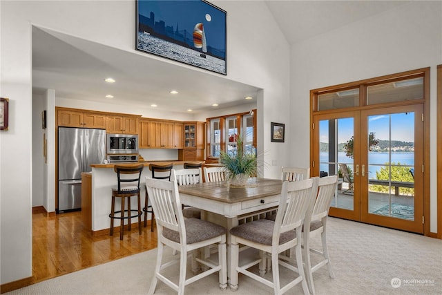 dining space featuring a high ceiling, a water view, light hardwood / wood-style flooring, and french doors