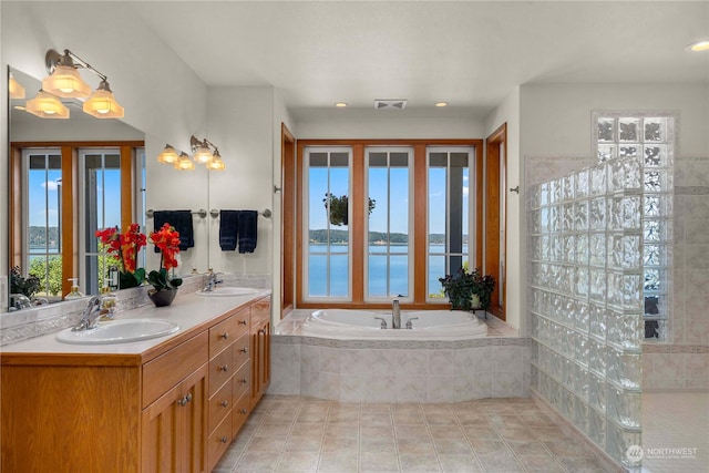 bathroom with tiled tub, a water view, a healthy amount of sunlight, and tile patterned flooring