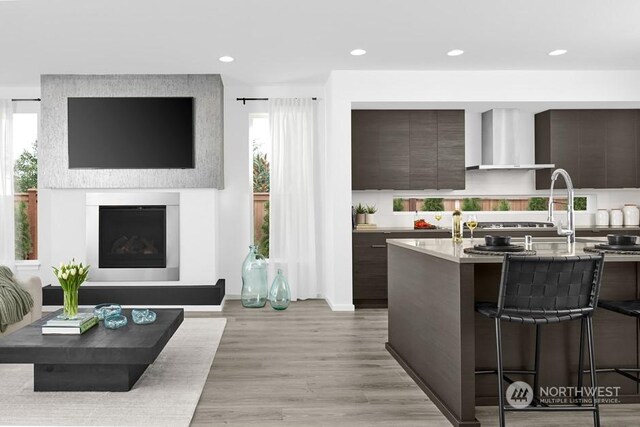 kitchen with dark brown cabinetry, a wealth of natural light, a breakfast bar, and wall chimney range hood